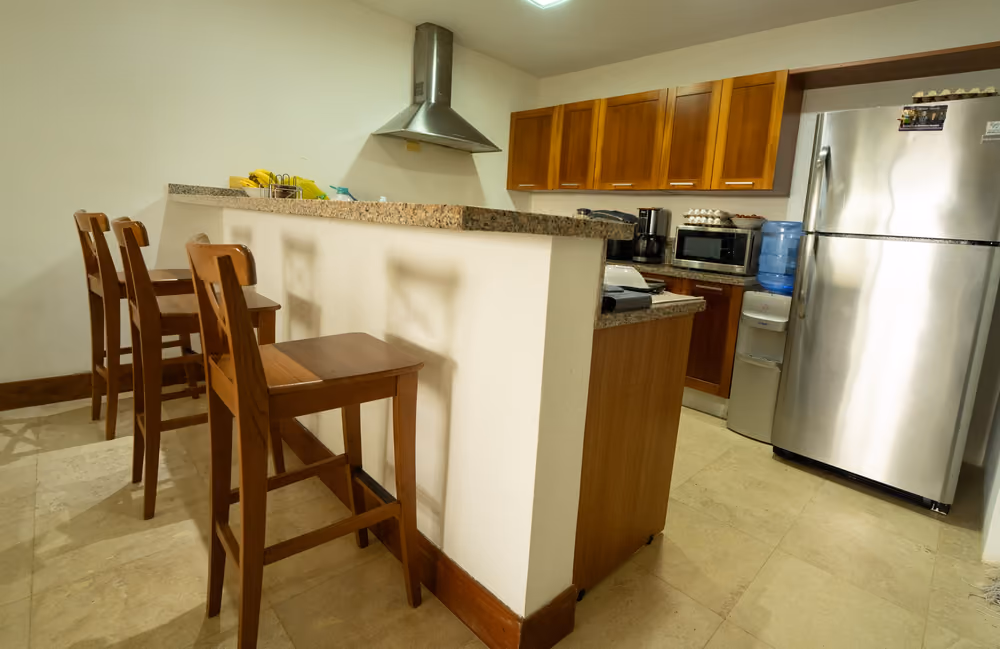 Cocina con barra desayunadora, gabinetes de madera y nevera de acero inoxidable