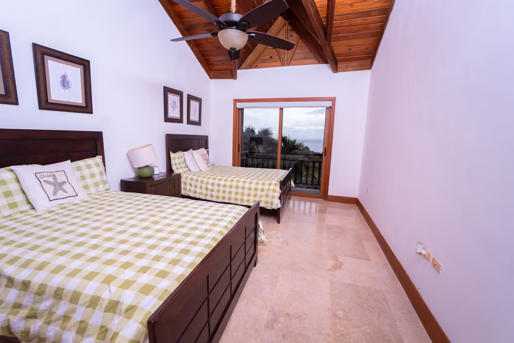 Segundo dormitorio con dos camas, techo de madera y balcón con vista a la bahía